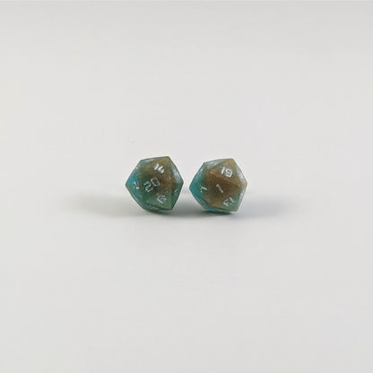 A single pair of the larger size handmade d20 earrings with titanium hardware that are teal and copper swirls with silver numbers on a white background. The earring on the left centers the 20 face and the earring on the right centers the 1 face.
