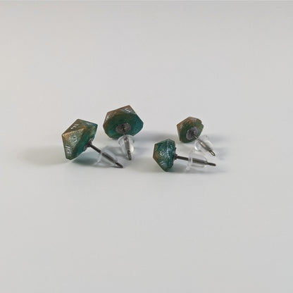 Two pairs of handmade d20 earrings that are teal and copper swirls with silver numbers turned to show the titanium hardware and bell shaped rubber backs.