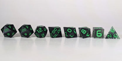 A straight on photo of a complete set of polyhedral dice that are black with some semitranslucent swirls and bright green numbers arranged in a straight line. They are lined up with the 2 d20s on the left going down to the d4 on the right side. The highest value number of each die is facing forward.