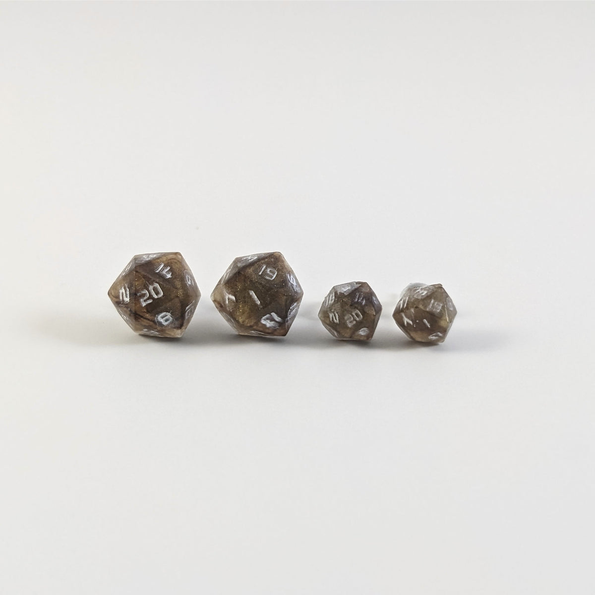 Two pairs of handmade d20 earrings with titanium hardware that are brown and yellow tiger's eye swirls with white numbers on a white background sit in a line with the larger pair on the left and the smaller pair on the right. The earrings on the left of each pair centers the 20 face and the earrings on the right of each pair centers the 1 face.