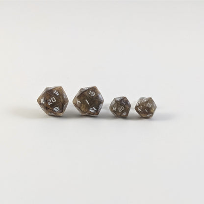 Two pairs of handmade d20 earrings with titanium hardware that are brown and yellow tiger's eye swirls with white numbers on a white background sit in a line with the larger pair on the left and the smaller pair on the right. The earrings on the left of each pair centers the 20 face and the earrings on the right of each pair centers the 1 face.