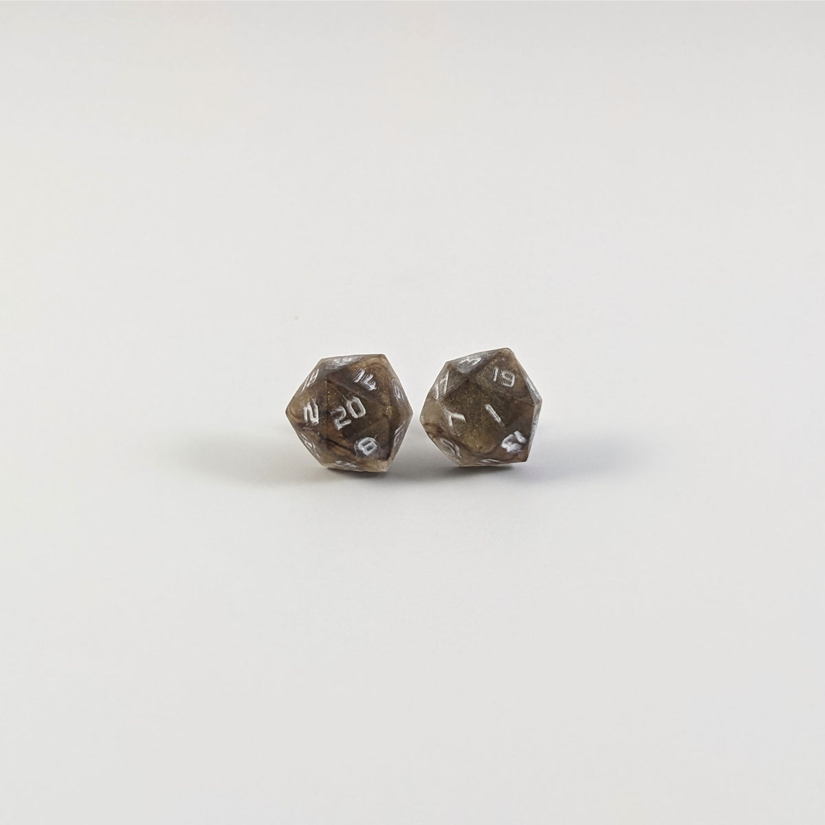 A single pair of the larger size handmade d20 earrings with titanium hardware that are brown and yellow tiger's eye swirls with white numbers on a white background. The earring on the left centers the 20 face and the earring on the right centers the 1 face.