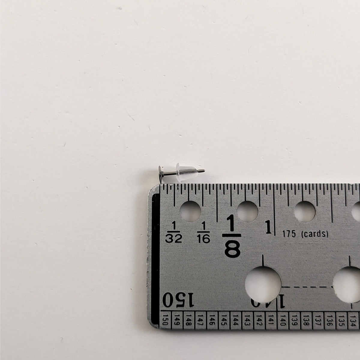 A size graphic of an earring post and bell shaped rubber back back next to a ruler and on a white background. It shows the length of the post as 10.3 mm or 0.40 in.