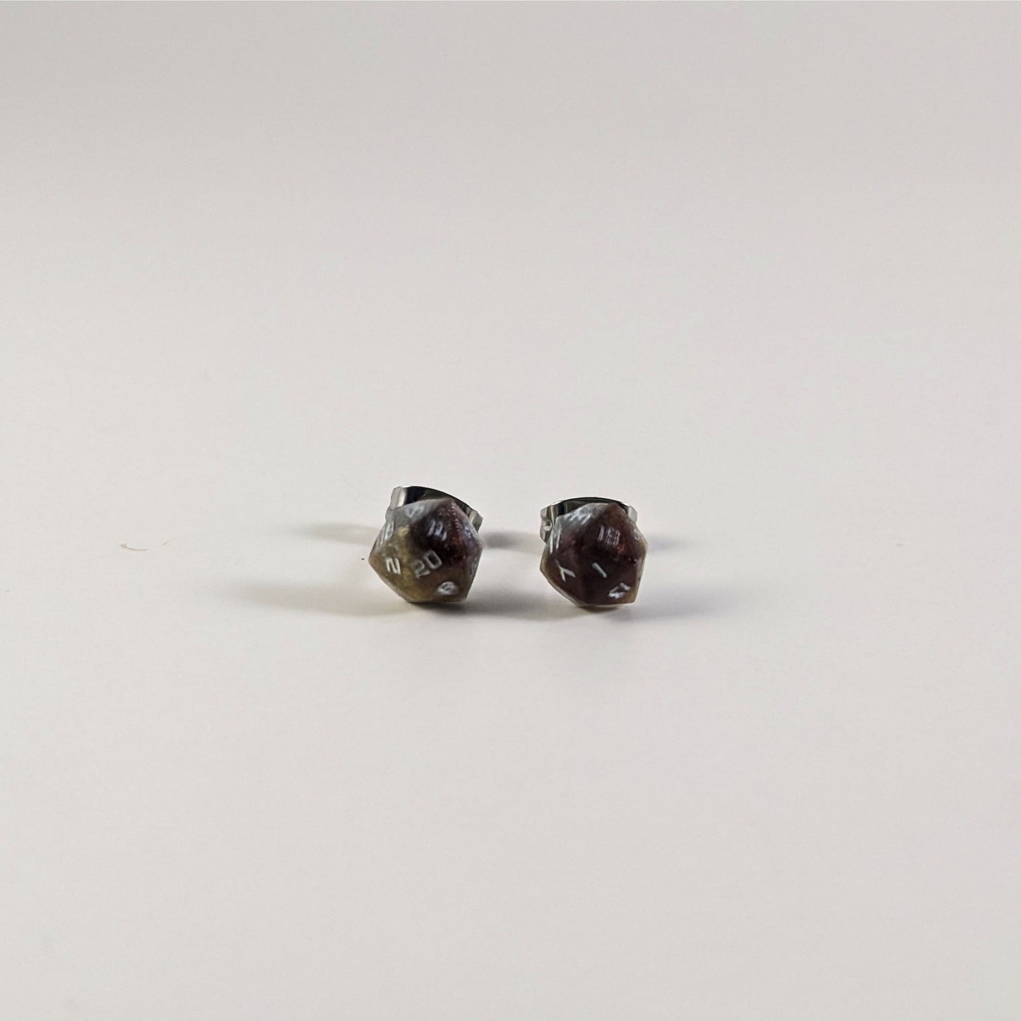 A single pair of the smaller size handmade d20 earrings that are maroon, dark silver, and gold with white numbers on a white background. The earring on the left centers the 20 face and the earring on the right centers the 1 face.