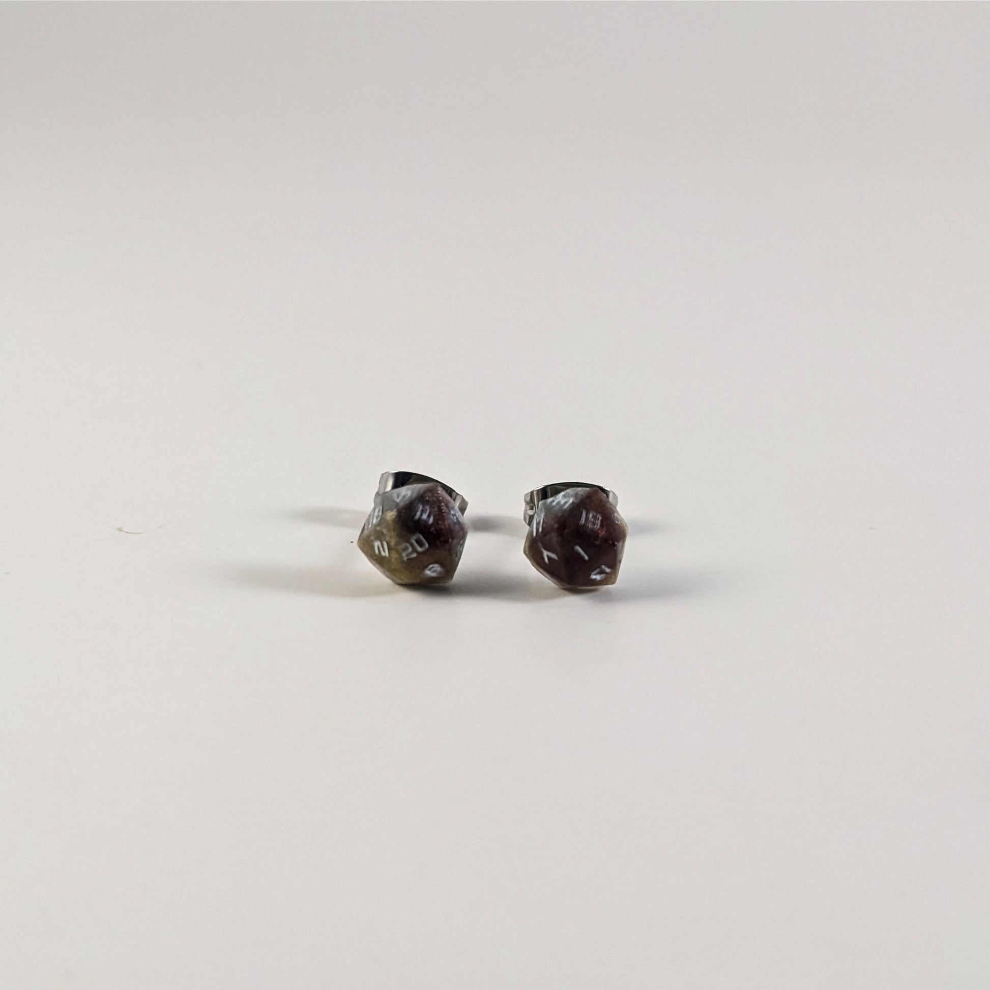 A single pair of the smaller size handmade d20 earrings that are maroon, dark silver, and gold with white numbers on a white background. The earring on the left centers the 20 face and the earring on the right centers the 1 face.