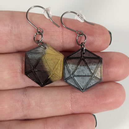 A pair of gold, maroon, and dark silver dangly, flat d20 earrings with silver color titanium and niobium hardware with bell shaped rubber backs held on on a hand on a white background.