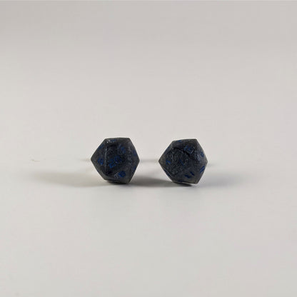 A single pair of the larger size handmade d20 earrings that are black and dark silver with blue numbers on a white background. The earring on the left centers the 20 face and the earring on the right centers the 1 face.