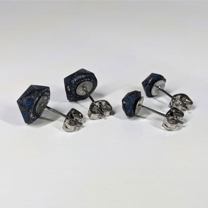 Two pairs of handmade d20 earrings that are black and dark silver with blue numbers turned to show the metal alloy hardware and butterfly backs.