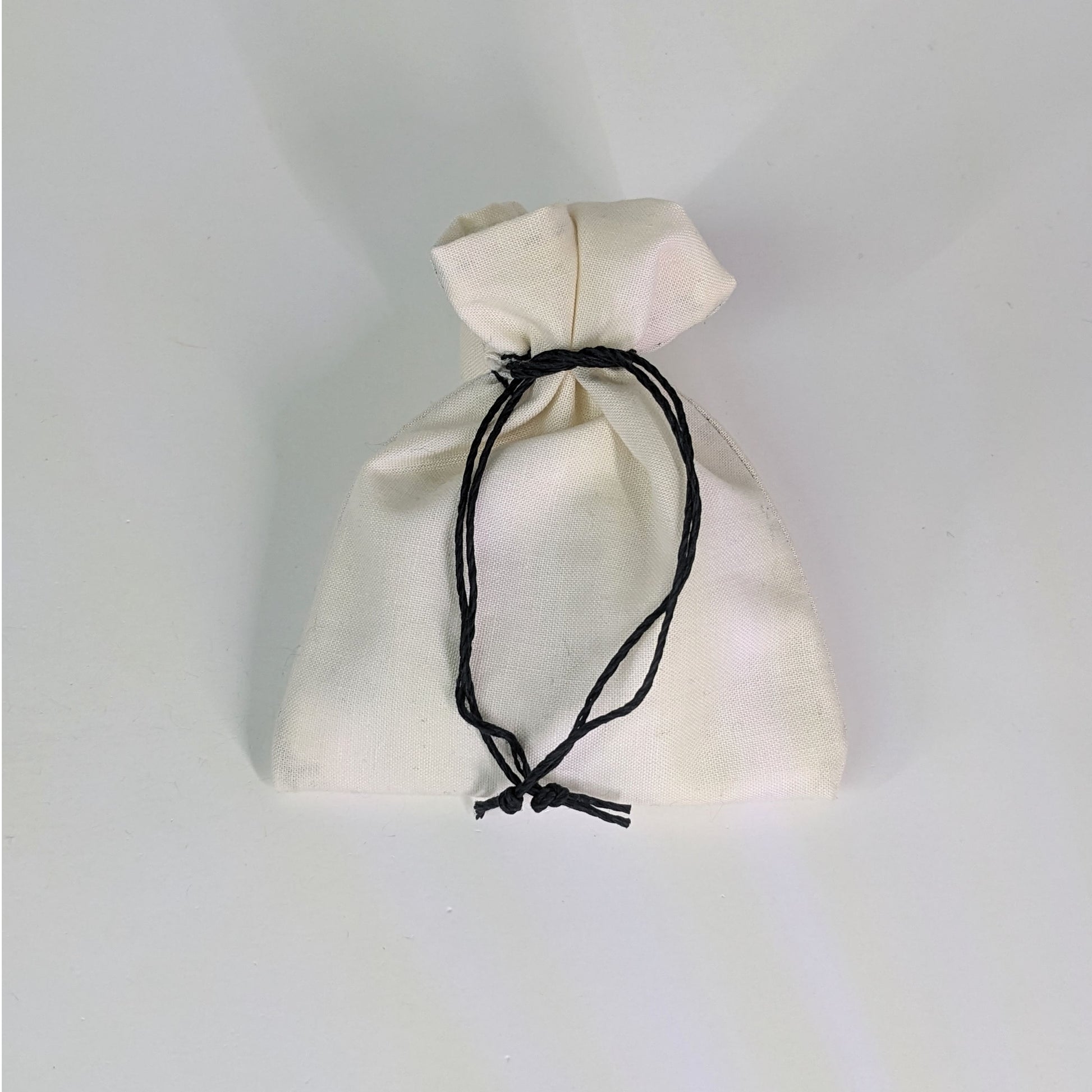 A small, handmade dice bag that is white is tied closed on a white background.