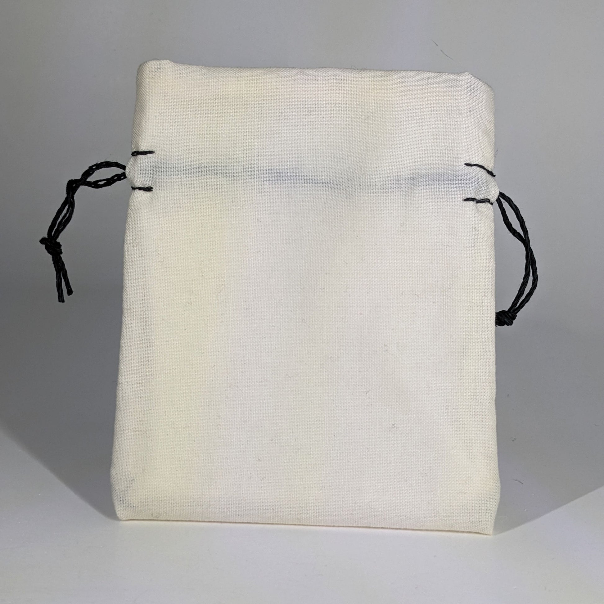 A small, handmade dice bag that is white stands upright on a white background.