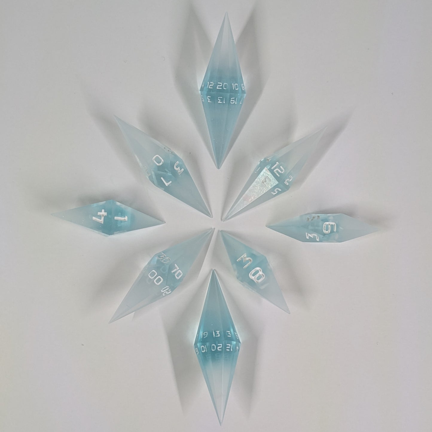 A complete set of resin dice featuring 2 d20s for advantage rolls. These mixed blue and white semitransparent with white numbering slender handmade diamond dice are clustered in a tight circle on a white background, highlighting the quality of the artisan dice craftsmanship and the unique pointed shape.