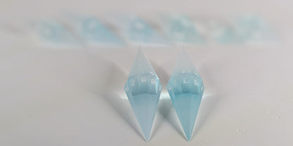 A stylized macro shot focusing heavily on 2 d20s from a mixed blue and white semitransparent with white numbering handmade dice set in the foreground. The sharp diamond edges of these front resin dice are crisp, while the rest of the matching artisan dice collection forms a softly blurred background, creating depth.