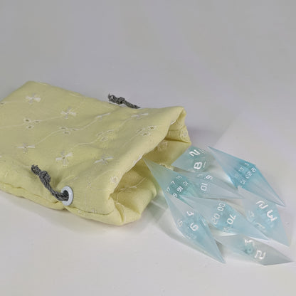 Mixed blue and white semitransparent with white numbering diamond handmade dice spilling out of a yellow patterned drawstring bag on a white background. The set features 2 d20s and matching resin dice, showcasing the unique shape of these artisan dice.
