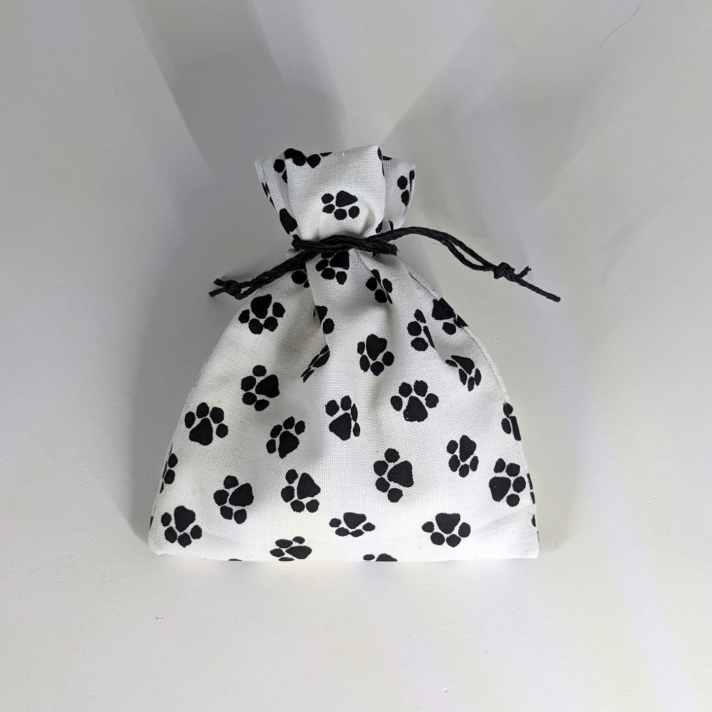 A small, handmade dice bag that is white with a black paw print pattern is tied closed on a white background.