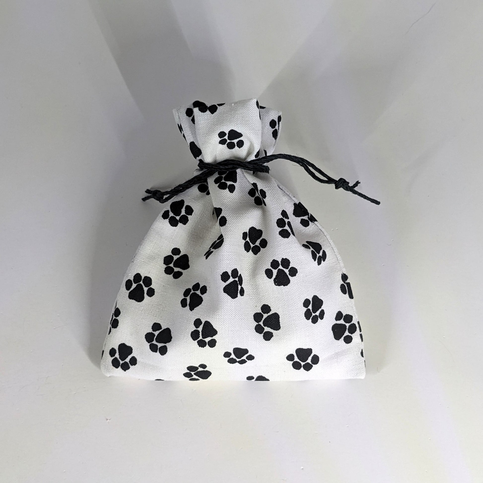 A small, handmade dice bag that is white with a black paw print pattern is tied closed on a white background.