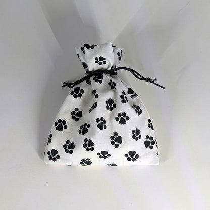 A small, handmade dice bag that is white with a black paw print pattern is tied closed on a white background.