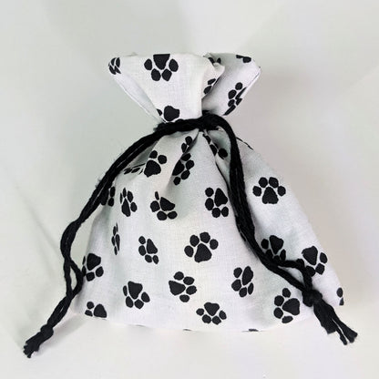 A small, handmade dice bag that is white with a black paw print pattern is tied closed on a white background.