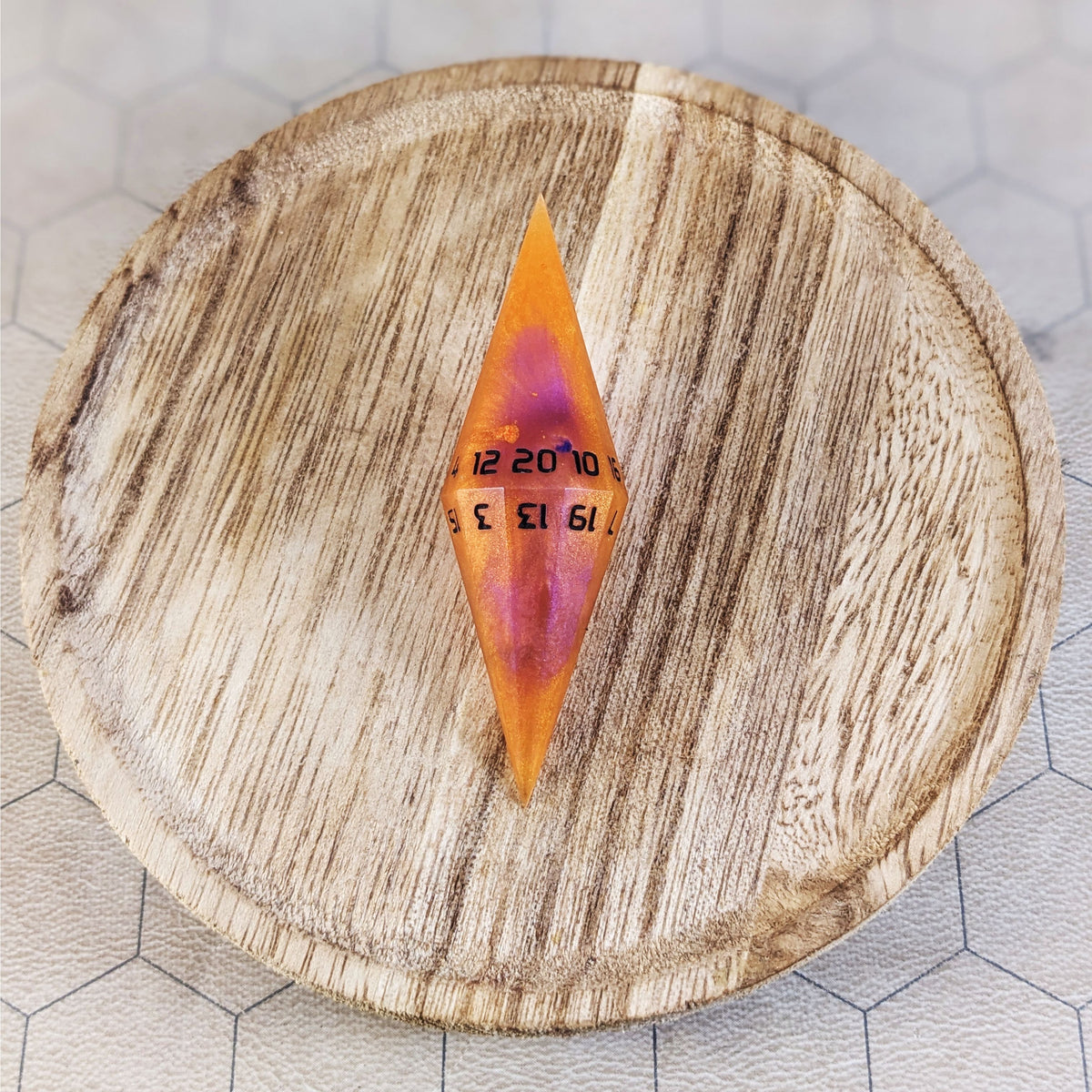 An orange and purple dagger d20 with black numbers sits in the center of a wooden circle on a beige hex map.