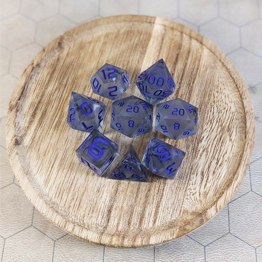 A complete set of 8 handmade artisan dice that have have black swirls around a cloudy spherical insert with purple numbers. The DnD dice set is on a wooded circle and the dice are arranged in a circle and features 2 D20s, one of which is in the center surrounded by the other 7 dice.