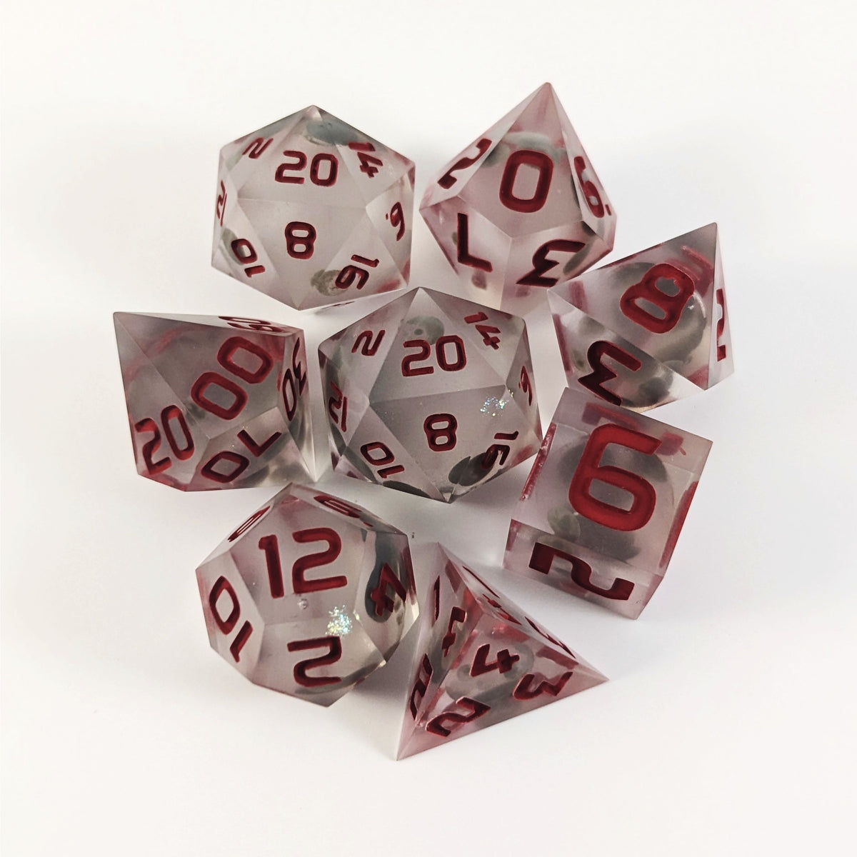 A complete set of 8 handmade artisan dice that have glow in the dark moon design inserts with red numbers. The DnD dice set is arranged in a circle and features 2 D20s, one of which is in the center surrounded by the other 7 dice on a white background.