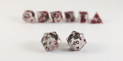 A straight on photo of a standard set of DnD dice that have glow in the dark moon design inserts with red numbers focusing on 2 d20s in the center. The d20 on the left has the 1 face centered and the d20 on the right has the 20 face centered. The other 6 dice are lined up in the background but are out of focus, while the d20s are in sharp focus.