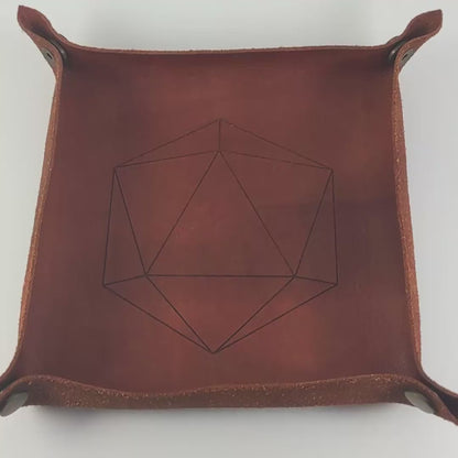 The video starts with a brown leather dice tray in view that has a d20 shape lasered into it. A hand appears from the bottom right corner holding a complete set of dagger dice that are green and black with orange numbers that glow in the dark. The hand rolls all of the dice into the tray from the right.