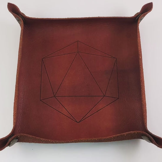 The video starts with a brown leather dice tray in view that has a d20 shape lasered into it. A hand enters from the bottom right corner holding a black and white marbled with a slight gold shimmer reliable talent d20 with gold numbers. The hand spins the d20 to show off how each face that is normally 9 or below is replaced with a 10. Then the hand rolls the die into the tray from the right. The die lands on a natural 20.
