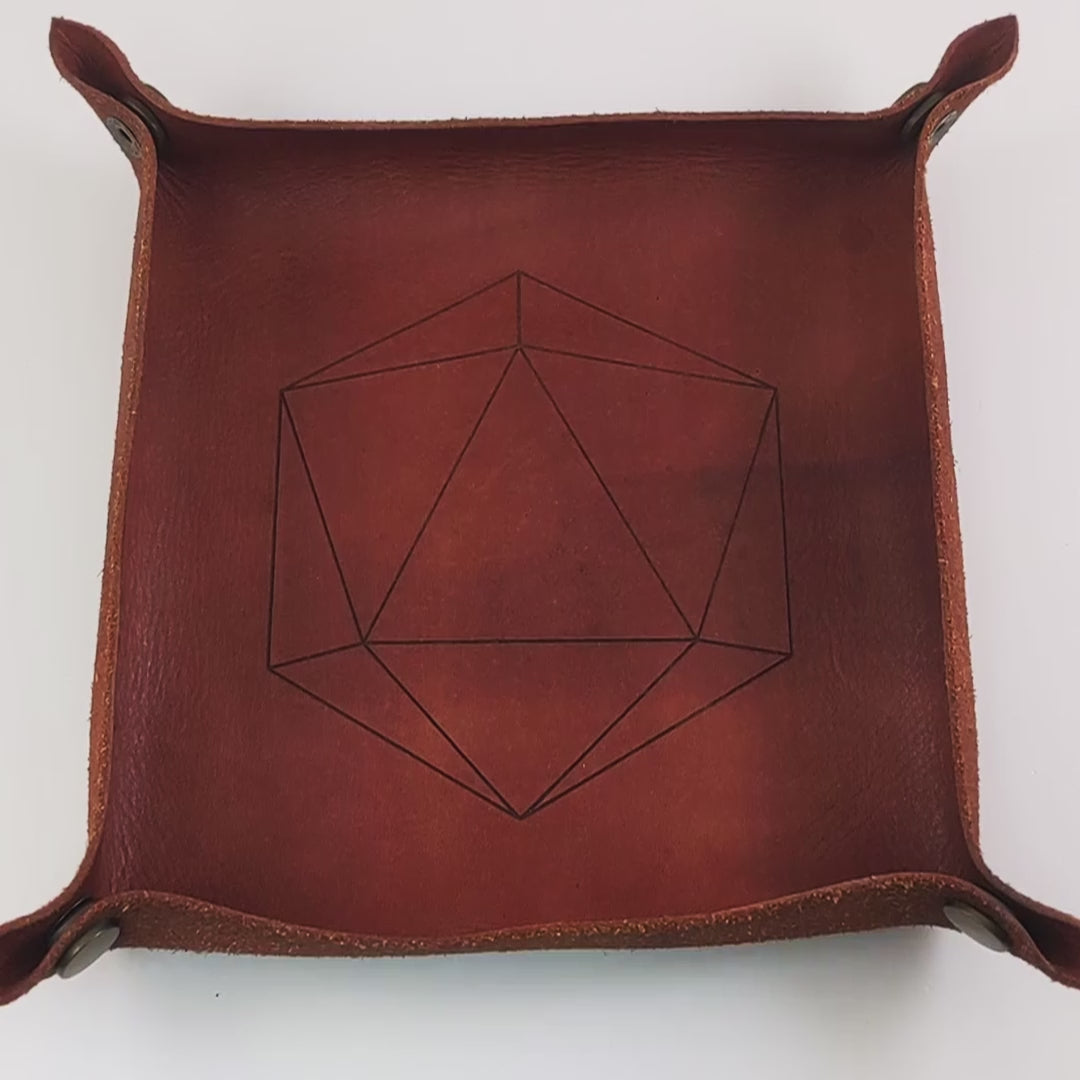 The video starts with a brown leather dice tray in view that has a d20 shape lasered into it. A hand enters from the bottom right corner holding a black and white marbled with a slight gold shimmer reliable talent d20 with gold numbers. The hand spins the d20 to show off how each face that is normally 9 or below is replaced with a 10. Then the hand rolls the die into the tray from the right. The die lands on a natural 20.