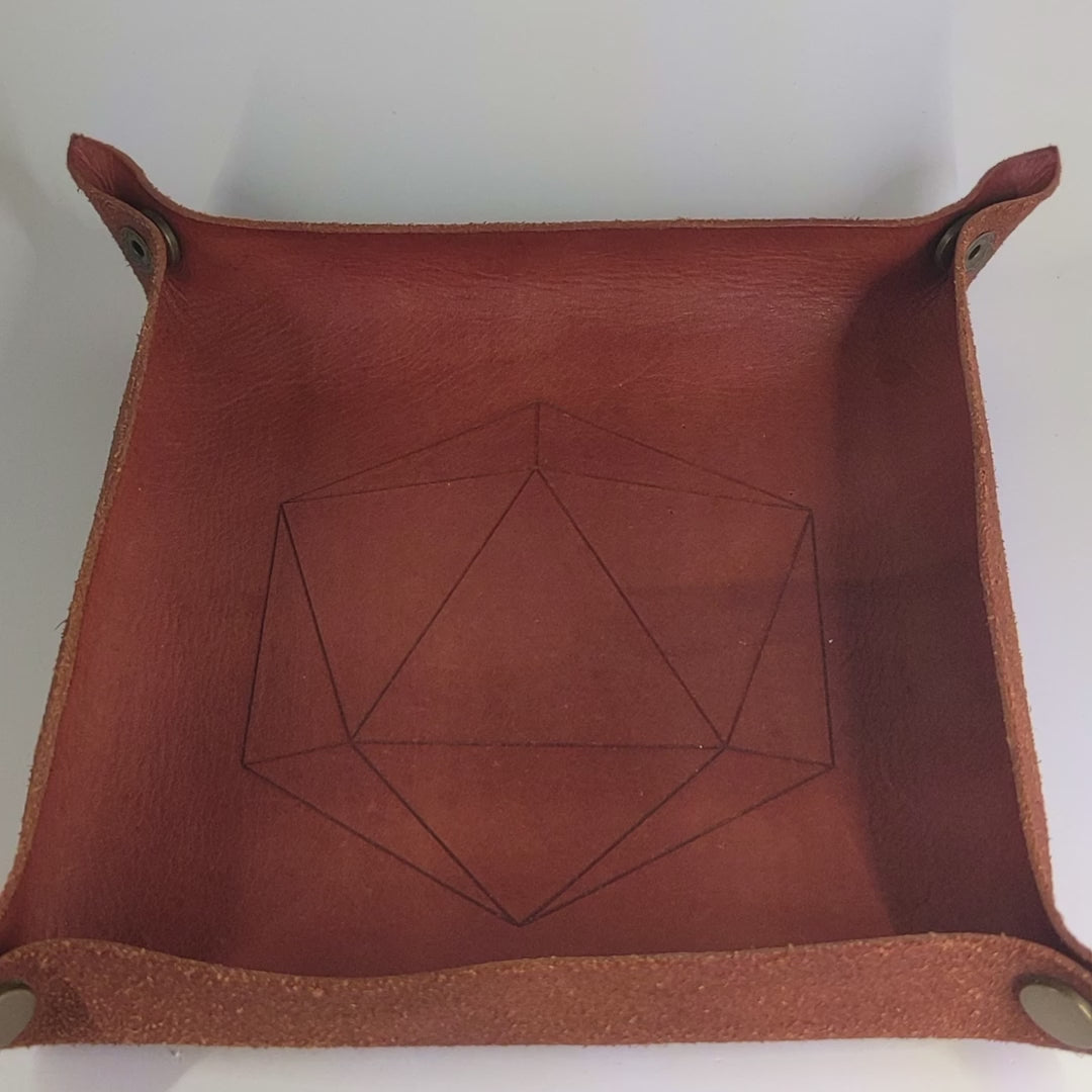 The video starts with a brown leather dice tray in view that has a d20 shape lasered into it. A hand rolls a complete set of glowy red-orange with dark spherical inserts and black numbers dice into the dice tray from the right.
