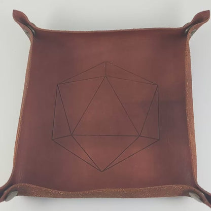 The video starts with a brown leather dice tray in view that has a d20 shape lasered into it. A hand appears from the bottom holding a diamond d20 that is black and green with purple numbers that glow in the dark. The hand rolls all of the dice into the tray from the right.