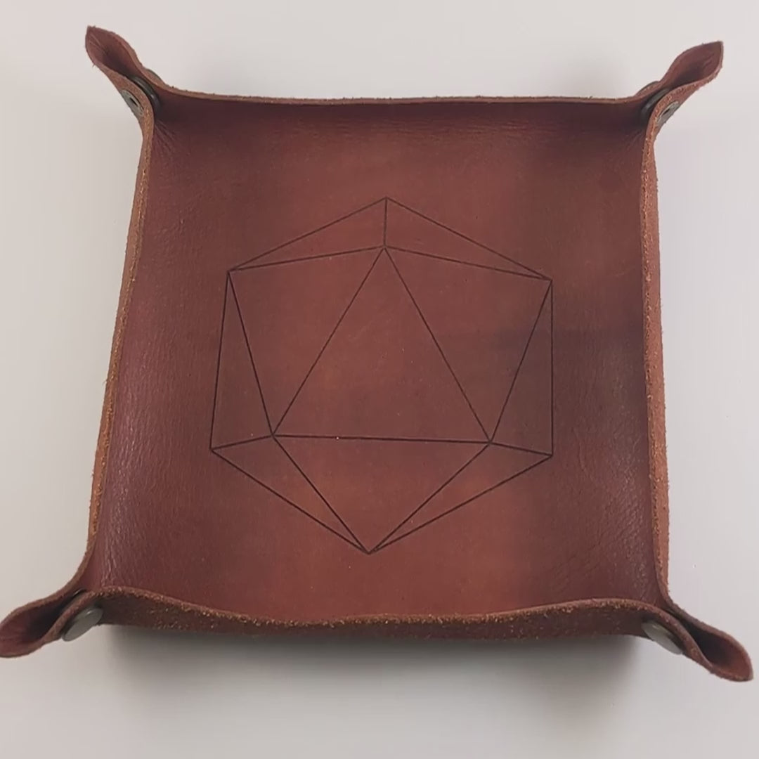 The video starts with a brown leather dice tray in view that has a d20 shape lasered into it. A hand appears from the bottom right corner holding a complete set of polyhedral dice that are icy blue with edges painted with white and iridescent glitter in a clear shell with white numbers. The hand rolls all of the dice into the tray from the right.