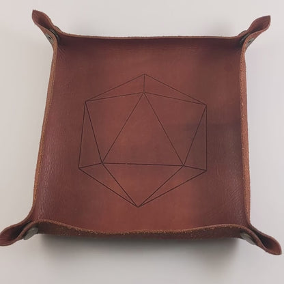 The video starts with a brown leather dice tray in view that has a d20 shape lasered into it. A hand appears from the bottom right corner holding a complete set of polyhedral dice that are icy blue with edges painted with white and iridescent glitter in a clear shell with white numbers. The hand rolls all of the dice into the tray from the right.
