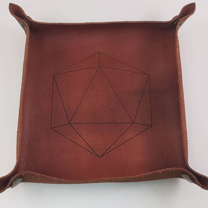 The video starts with a brown leather dice tray in view that has a d20 shape lasered into it. A hand enters from the bottom right corner holding a light green reliable talent d20 with gold numbers. The hand spins the d20 to show off how each face that is normally 9 or below is replaced with a 10. Then the hand rolls the die into the tray from the right.