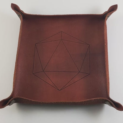 The video starts with a brown leather dice tray in view that has a d20 shape lasered into it. A hand appears from the bottom right corner holding a complete set of coffee brown with milky white swirls polyhedral dice with teal numbers. The hand rolls all of the dice into the tray from the right. One of the d20s lands on a natural 20.