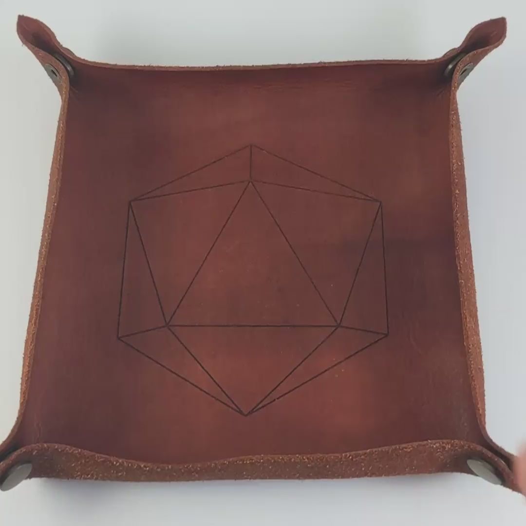 The video starts with a brown leather dice tray in view that has a d20 shape lasered into it. A hand appears from the bottom right corner holding a complete set of polyhedral dice that have  black swirls around a cloudy, spherical insert and purple numbers. The hand rolls all of the dice into the tray from the right.