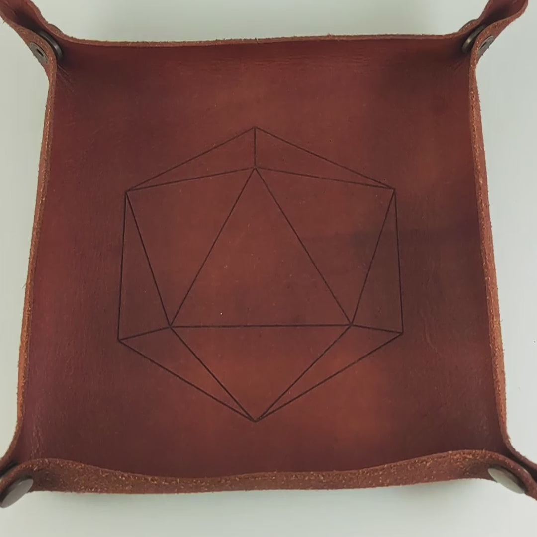 The video starts with a brown leather dice tray in view that has a d20 shape lasered into it. A hand appears from the right side holding a complete set of diamond dice that are swirling shades of green with black numbers. The hand rolls all of the dice into the tray from the right.