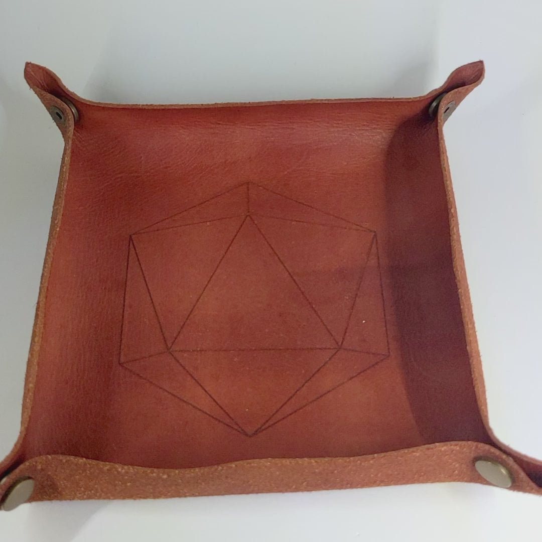 The video starts with a brown leather dice tray in view that has a d20 shape lasered into it. A hand rolls a complete set of purple, pink, and blue galaxy swirls with an extra touch of glitter and white numbers dagger dice into the dice tray from the right.