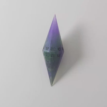 A video of a diamond d20 with swirls of purple and green with black numbers that glow in the dark on a white background. This transitions from light to darkness to show the black numbers glowing green in the dark.