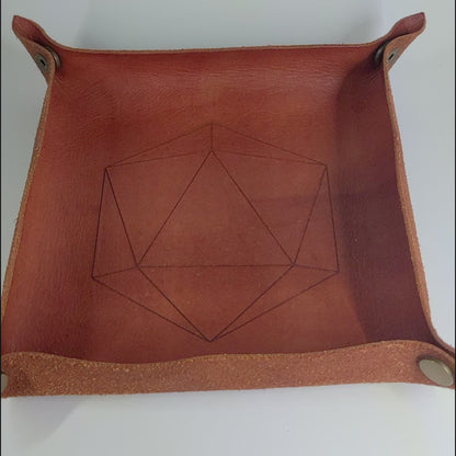 The video starts with a brown leather dice tray in view that has a d20 shape lasered into it. A hand appears from the right holding a complete set of polyhedral dice that have dark, spherical inserts with swirls of red in the shell and red numbers. The hand rolls all of the dice into the tray from the right.