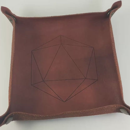 The video starts with a brown leather dice tray in view that has a d20 shape lasered into it. A hand appears from the bottom right corner holding a complete set of polyhedral dice that are purple with black cat designs with bright green numbers. The hand rolls all of the dice into the tray from the right. One of the d20s lands on a natural 20, the other lands on a natural 1.