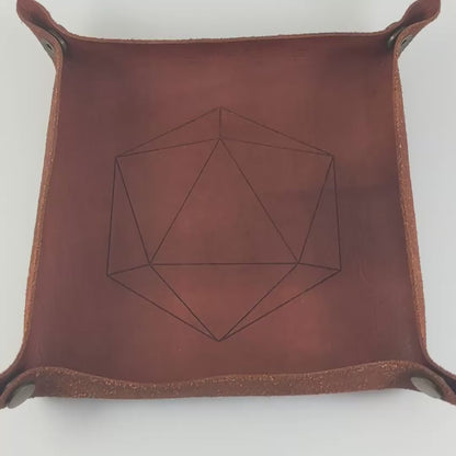 The video starts with a brown leather dice tray in view that has a d20 shape lasered into it. A hand appears from the bottom right corner holding a complete set of polyhedral dice that  have jack-o-lantern inserts whose faces glow in the dark with dark green numbers. The hand rolls all of the dice into the tray from the right.