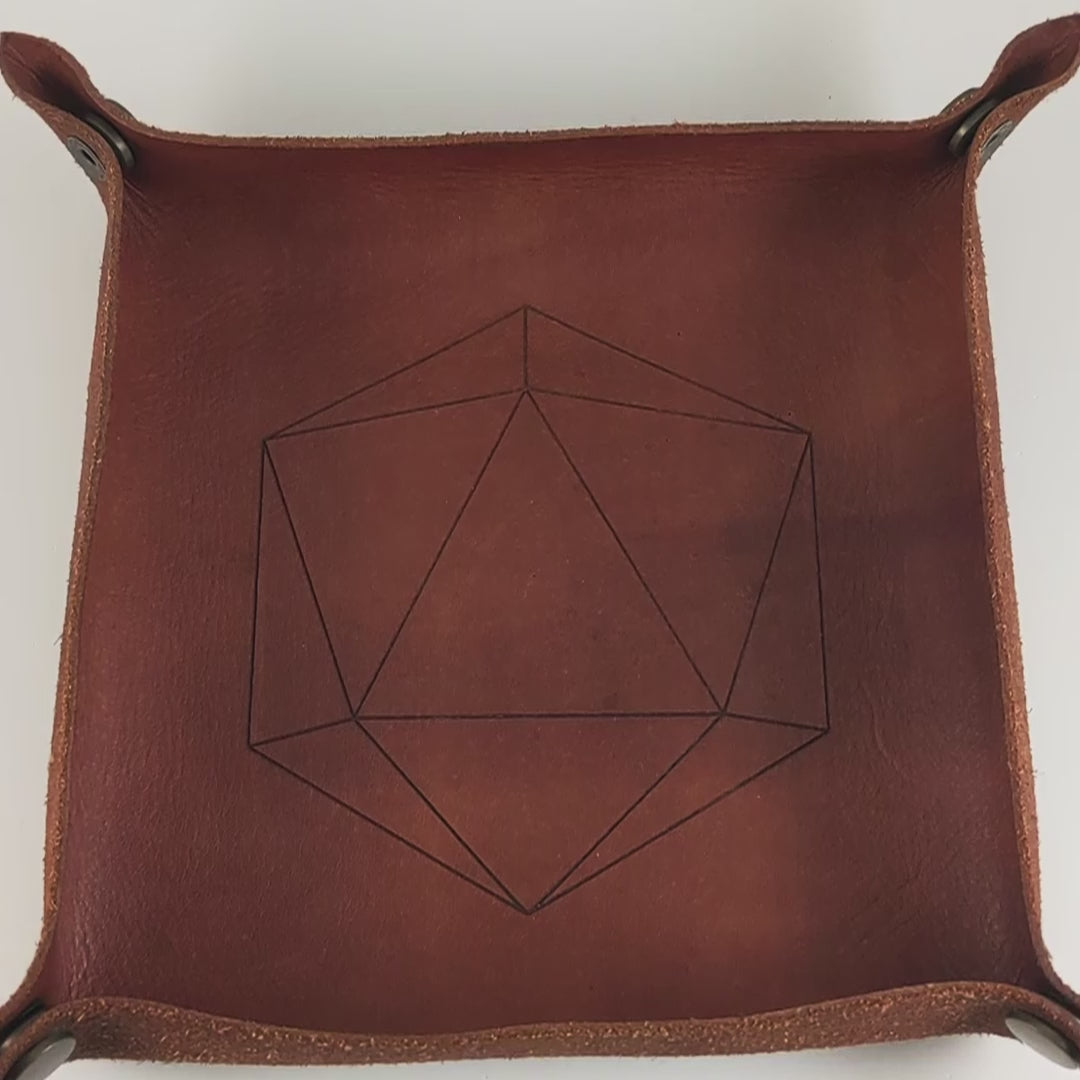 The video starts with a brown leather dice tray in view that has a d20 shape lasered into it. A hand appears from the bottom right corner holding a complete set of dagger dice that are bright orange tempered with deep red like cooling lava with obsidian black numbers. The hand rolls all of the dice into the tray from the right.