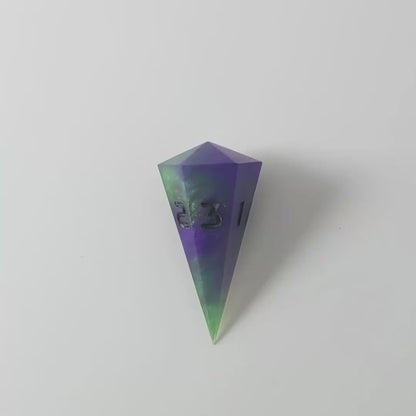 A video of a dagger d3 with swirls of purple and green with black numbers that glow in the dark on a white background. This transitions from light to darkness to show the black numbers glowing green in the dark.