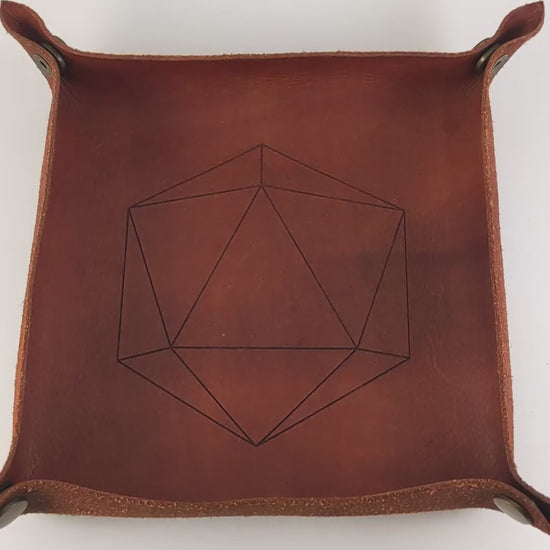 The video starts with a brown leather dice tray in view that has a d20 shape lasered into it. A hand appears from the bottom right corner holding a complete set of diamond dice that are shimmering gold and red gold swirls and red numbers. The hand rolls all of the dice into the tray from the right. One of the d20s rolls a natural 20.