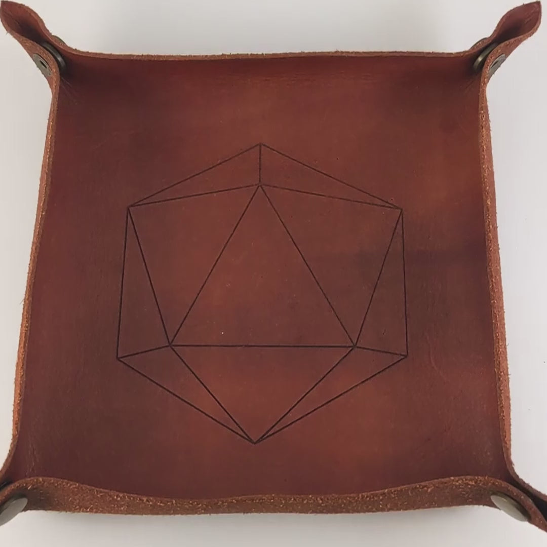 The video starts with a brown leather dice tray in view that has a d20 shape lasered into it. A hand appears from the bottom right corner holding a complete set of diamond dice that are shimmering gold and red gold swirls and red numbers. The hand rolls all of the dice into the tray from the right. One of the d20s rolls a natural 20.