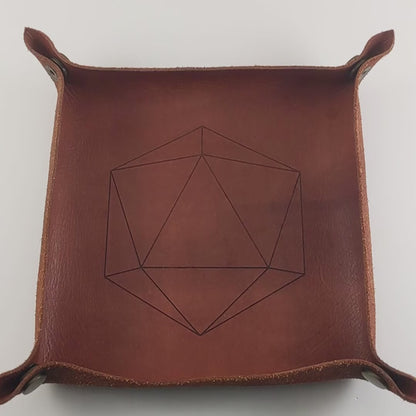 The video starts with a brown leather dice tray in view that has a d20 shape lasered into it. A hand appears from the bottom right corner holding up 5 dark green and black dagger shaped d6s that have red numbers to the camera. The hand rolls the dice into the dice tray from the right.