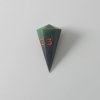 A video of a dagger d3 with swirls of black and green with orange numbers that glow in the dark on a white background. This transitions from light to darkness to show the black numbers glowing green in the dark.