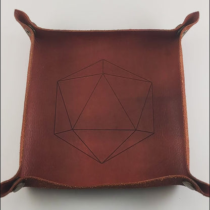 The video starts with a brown leather dice tray in view that has a d20 shape lasered into it. A hand appears from the bottom right corner holding 10 orange and red d6s to the camera. The hand rolls the dice from the right into the dice tray.