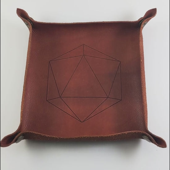 The video starts with a brown leather dice tray in view that has a d20 shape lasered into it. A hand appears from the bottom right corner holding a complete set of teal polyhedral dice with a pearlescent shine and copper numbers. The hand rolls all of the dice into the tray from the right.