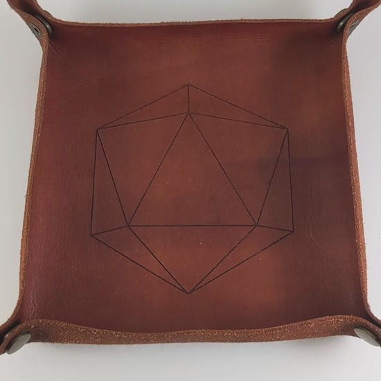 The video starts with a brown leather dice tray in view that has a d20 shape lasered into it. A hand appears from the bottom right corner holding a complete set of diamond dice that are shadowy swirls of black and silver with acidic green numbers. The hand rolls all of the dice into the tray from the right.